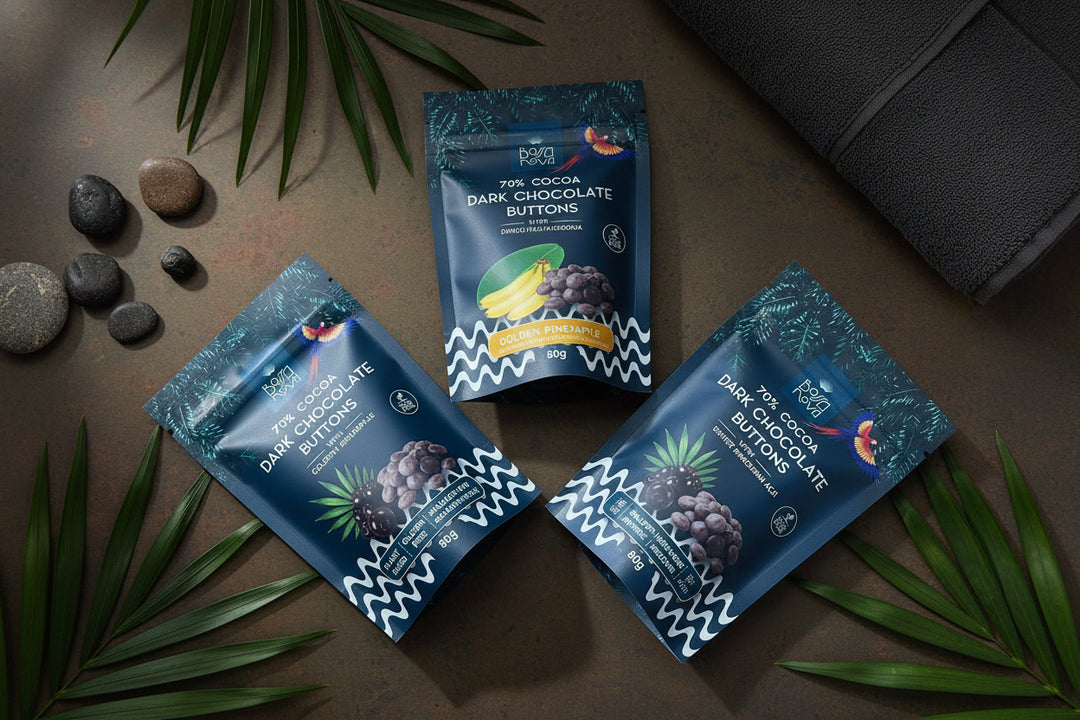 Three stand-up pouches of dark chocolate buttering paper packets arranged on a wooden floor. The packaging is dark blue with white zigzag borders, fruit illustrations, and text including 'Dark Chocolate Buttering Pouches' and '70% Dark Chocolate'.